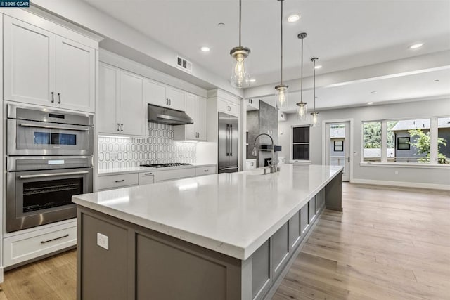 kitchen featuring pendant lighting, a large island with sink, and white cabinets