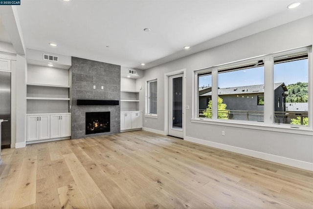 unfurnished living room with a fireplace, built in features, and light hardwood / wood-style flooring