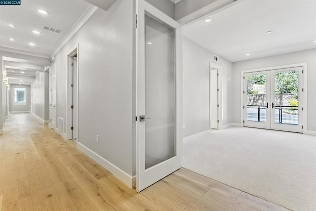 hall featuring light wood-type flooring, french doors, a wealth of natural light, and crown molding