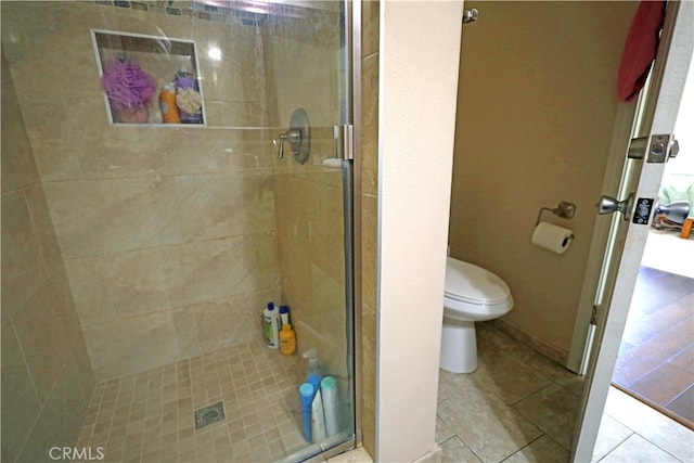 bathroom with tile patterned floors, a shower with door, and toilet