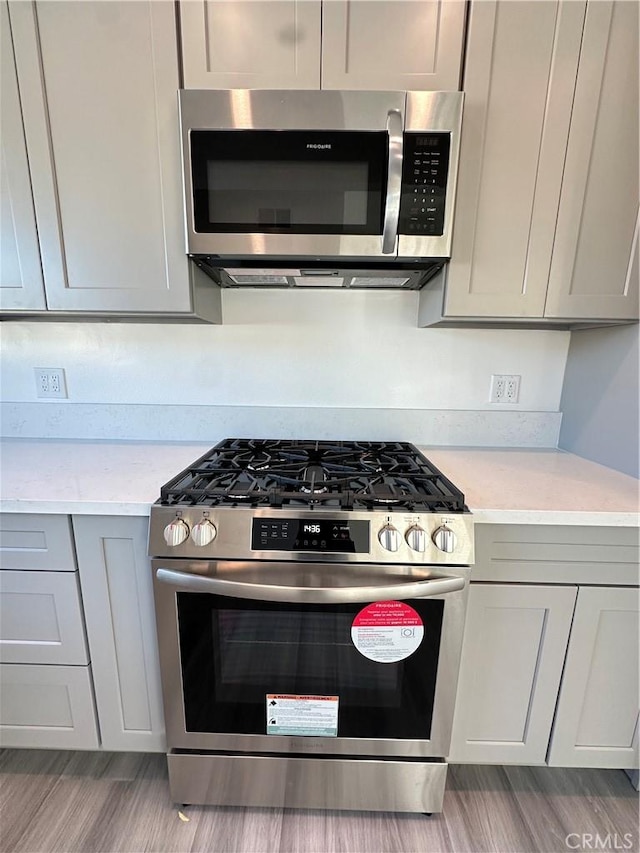 kitchen with appliances with stainless steel finishes, light hardwood / wood-style floors, and gray cabinetry