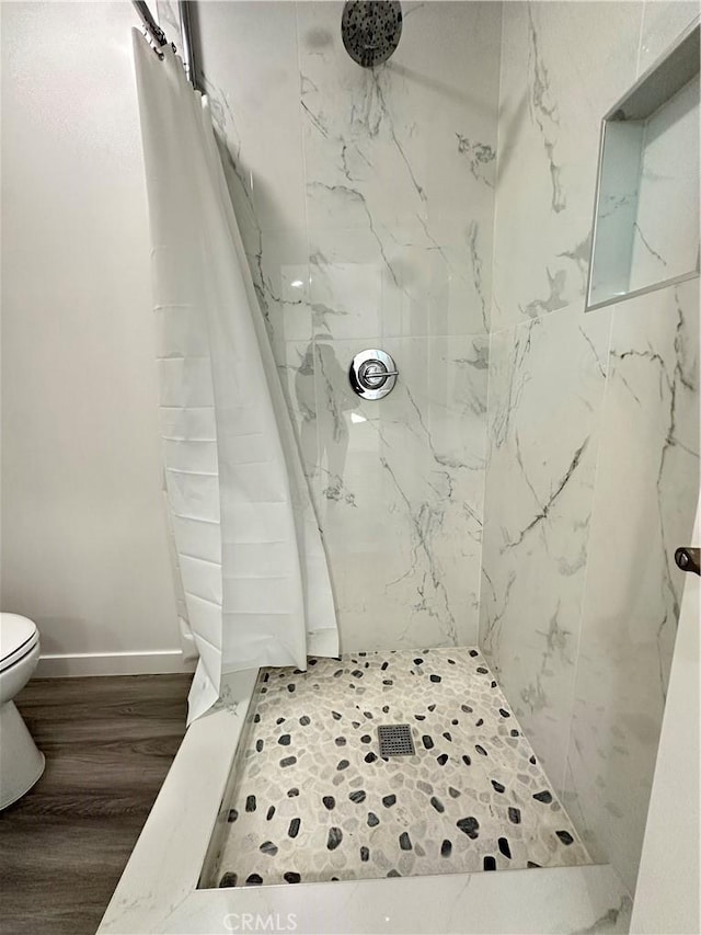 bathroom featuring toilet, a tile shower, and wood-type flooring