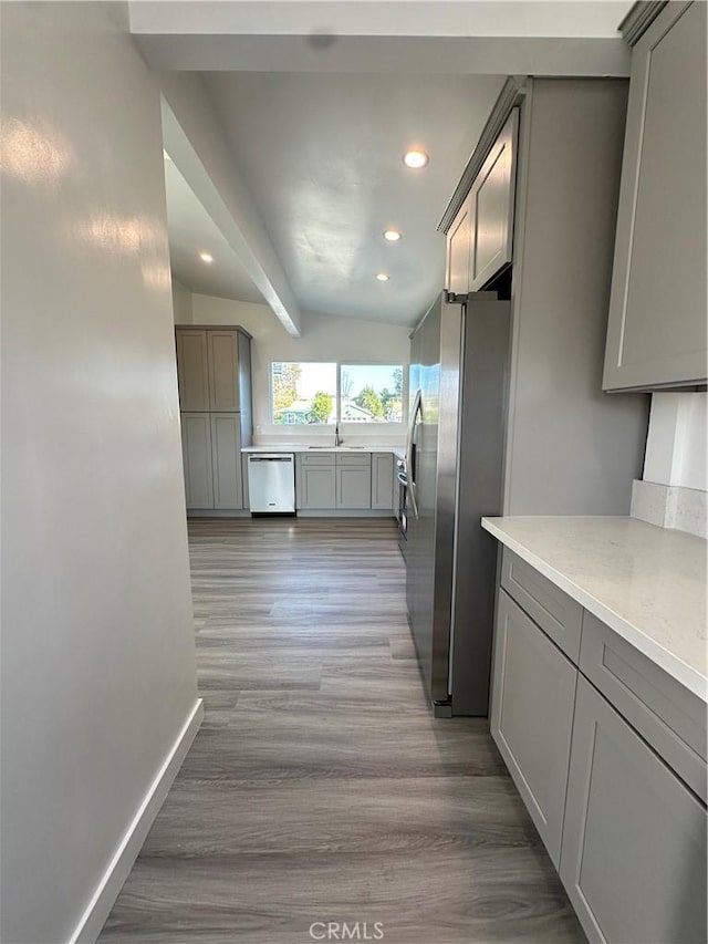 kitchen with gray cabinetry, lofted ceiling with beams, stainless steel appliances, and light hardwood / wood-style flooring