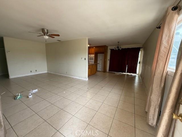 24062 Eucalyptus Ave, Moreno Valley, CA 92553 - unfurnished living room featuring ceiling fan with notable chandelier, light tile patterned floors, and a wealth of natural light