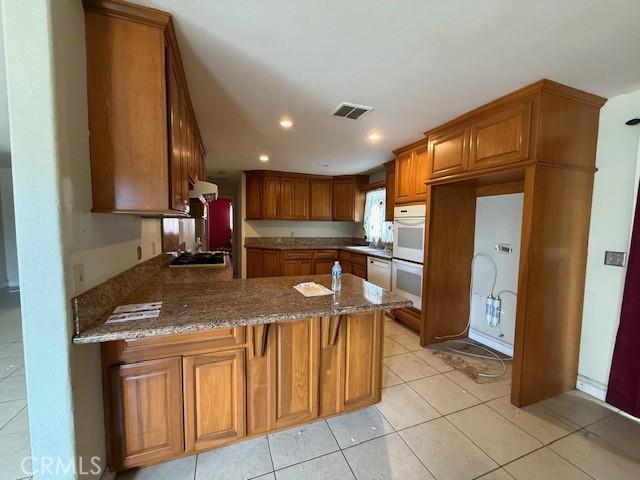 24062 Eucalyptus Ave, Moreno Valley, CA 92553 - kitchen featuring white appliances, brown cabinetry, dark stone counters, a peninsula, and visible vents