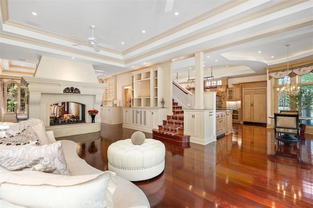 living room with ceiling fan with notable chandelier, a tray ceiling, dark hardwood / wood-style floors, and crown molding