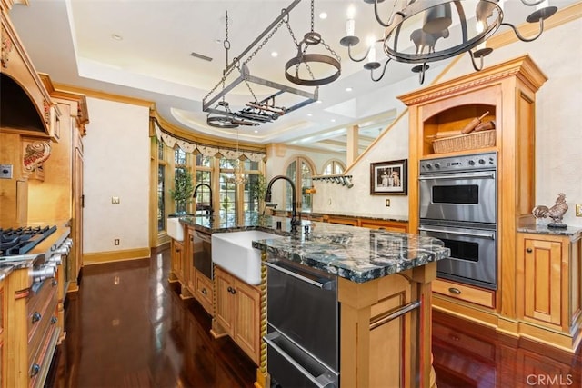 kitchen with dark wood-type flooring, dark stone counters, an island with sink, appliances with stainless steel finishes, and a chandelier