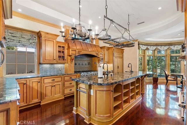 kitchen featuring decorative backsplash, a raised ceiling, a kitchen island with sink, and dark stone countertops