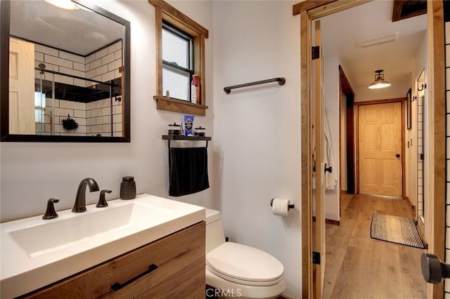 bathroom featuring a tile shower, vanity, hardwood / wood-style floors, and toilet