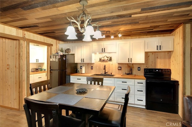 kitchen featuring stainless steel fridge, black range with electric stovetop, white cabinets, decorative light fixtures, and sink