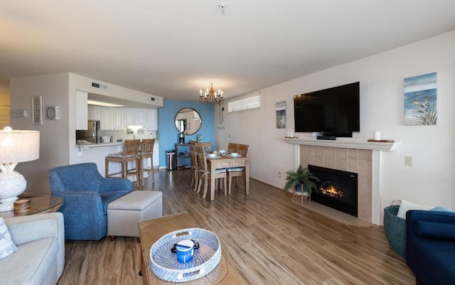 living room featuring a tiled fireplace, an inviting chandelier, and light wood-type flooring