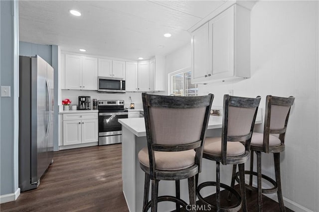 kitchen featuring dark wood-type flooring, stainless steel appliances, a kitchen bar, and white cabinetry