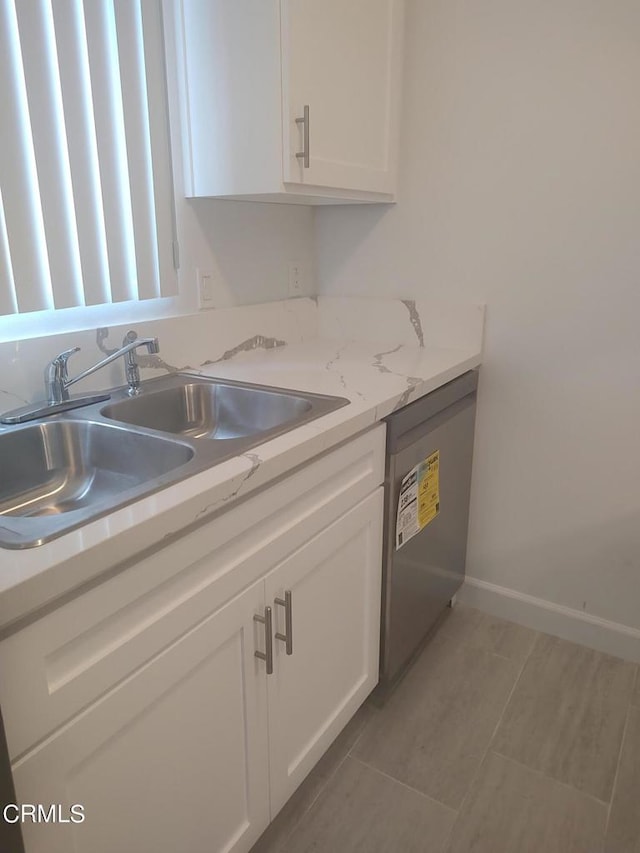 kitchen featuring light stone countertops, stainless steel dishwasher, sink, and white cabinetry