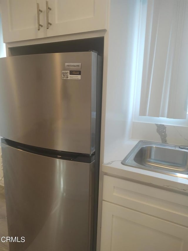 room details featuring stainless steel refrigerator, sink, and white cabinets