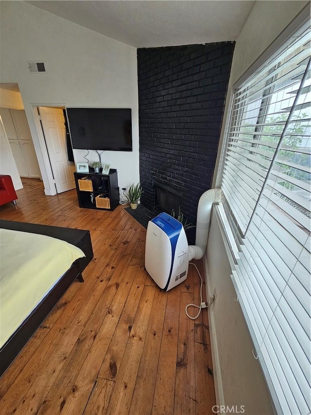 bedroom with light hardwood / wood-style floors, a brick fireplace, and lofted ceiling