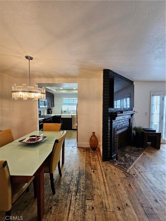 dining area with a textured ceiling, sink, wood-type flooring, a fireplace, and a chandelier