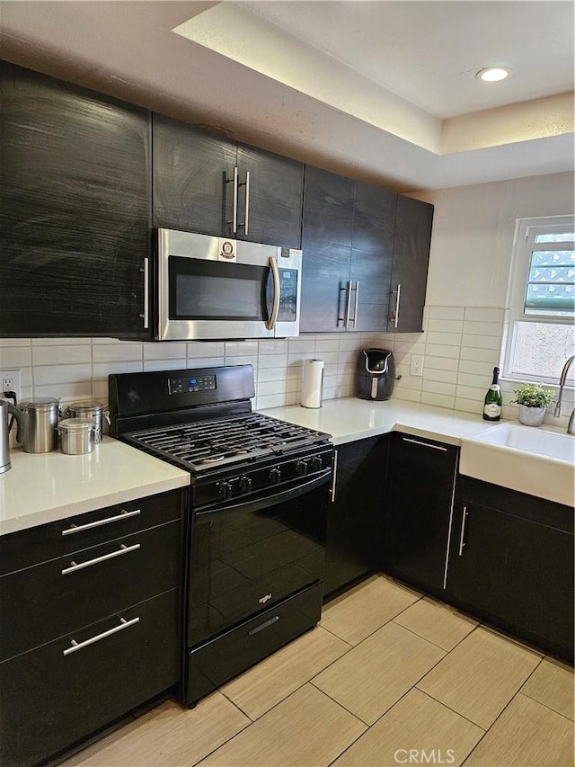 kitchen featuring a raised ceiling, decorative backsplash, black range with gas stovetop, and sink