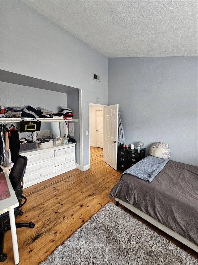 bedroom with lofted ceiling, a textured ceiling, and hardwood / wood-style flooring