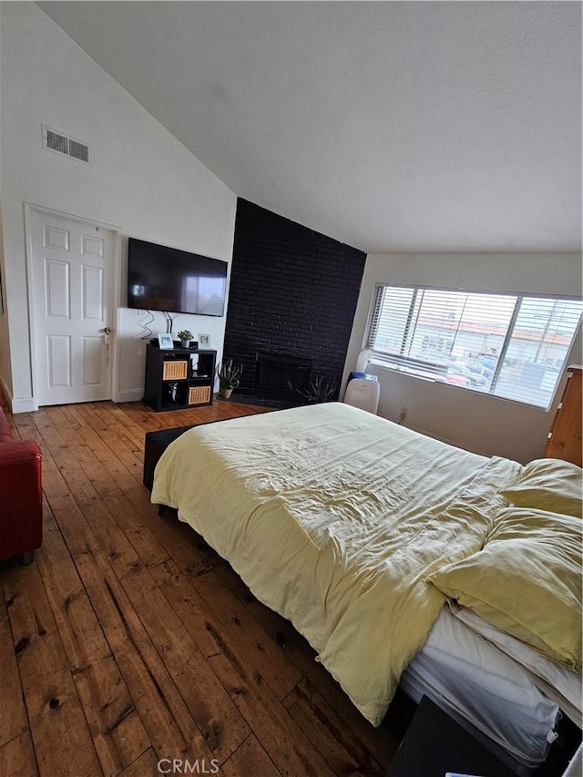 bedroom featuring hardwood / wood-style floors, vaulted ceiling, and a brick fireplace