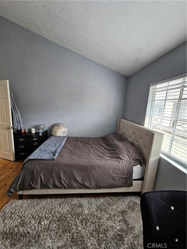 bedroom featuring vaulted ceiling, hardwood / wood-style floors, and a textured ceiling