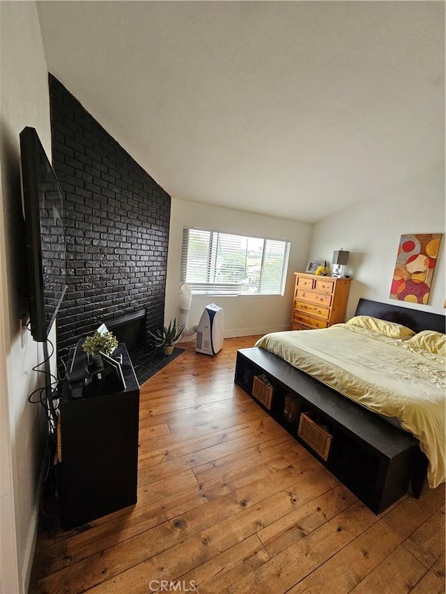 bedroom with light hardwood / wood-style floors, lofted ceiling, and a brick fireplace