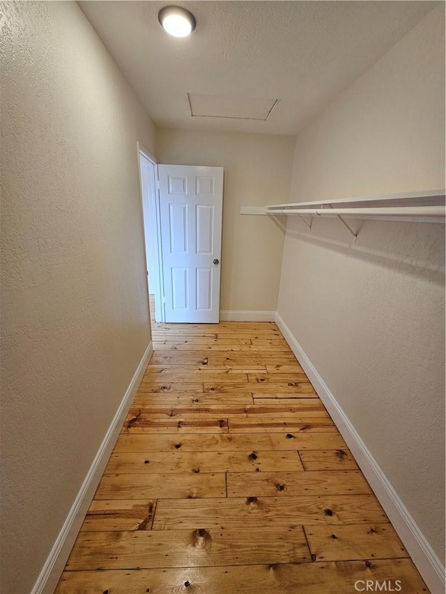 walk in closet with light wood-style flooring and attic access