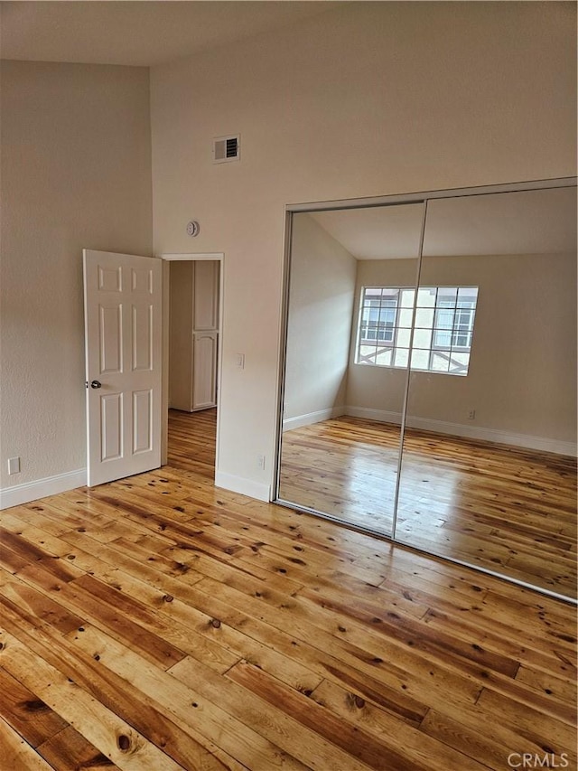 unfurnished bedroom featuring hardwood / wood-style flooring, baseboards, visible vents, and a closet