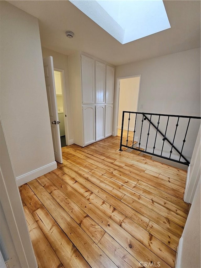 interior space featuring baseboards, an upstairs landing, a skylight, and light wood finished floors