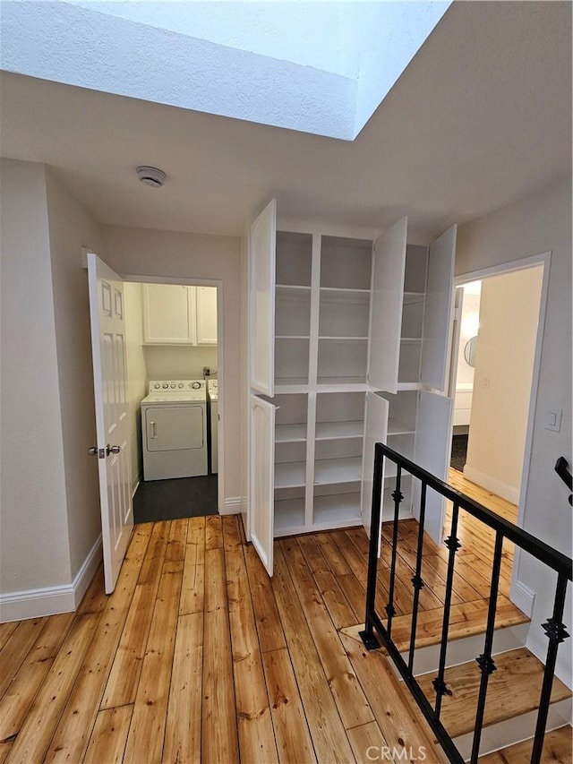 hallway with a skylight, separate washer and dryer, baseboards, and light wood finished floors