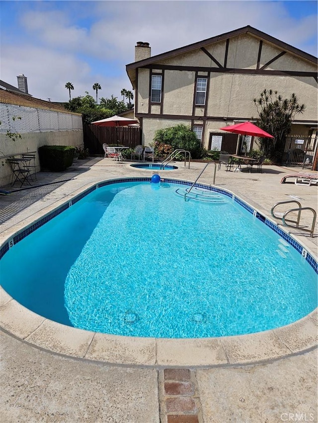 pool featuring a community hot tub, a patio area, and fence