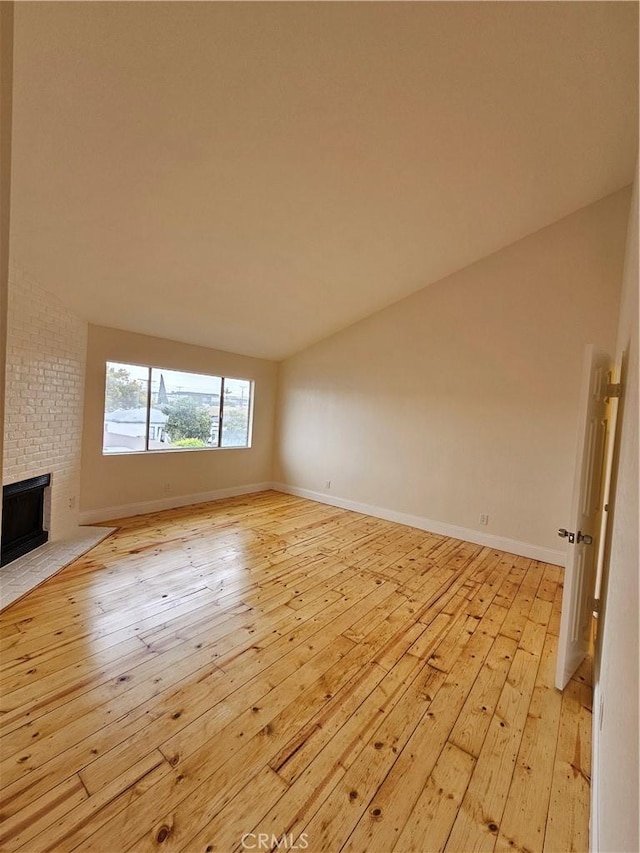 unfurnished living room featuring vaulted ceiling, a fireplace, light wood-type flooring, and baseboards