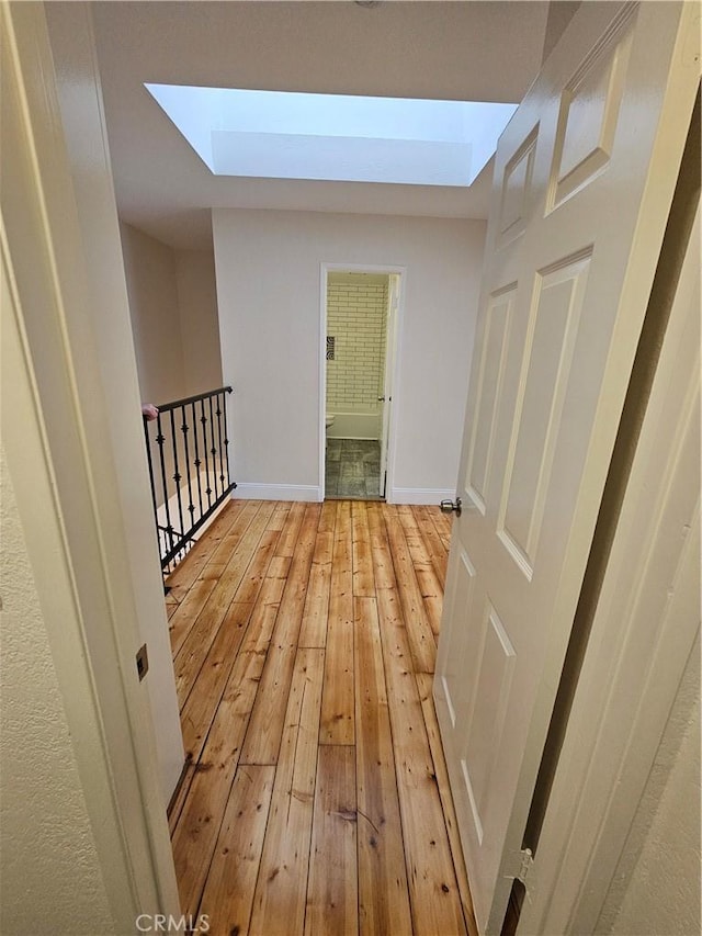 hallway with an upstairs landing, light wood-style flooring, a skylight, and baseboards