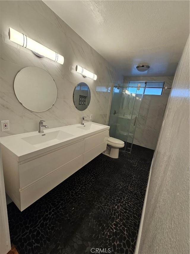 full bathroom with a stall shower, a sink, a textured ceiling, tile walls, and toilet