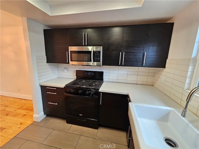 kitchen featuring tasteful backsplash, stainless steel microwave, black range with gas stovetop, light countertops, and a sink