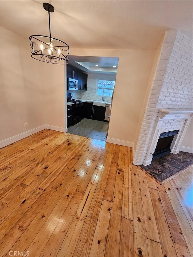 unfurnished dining area with a brick fireplace, a notable chandelier, light wood-style floors, and baseboards