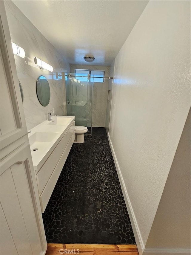 bathroom featuring toilet, a sink, a shower stall, double vanity, and baseboards