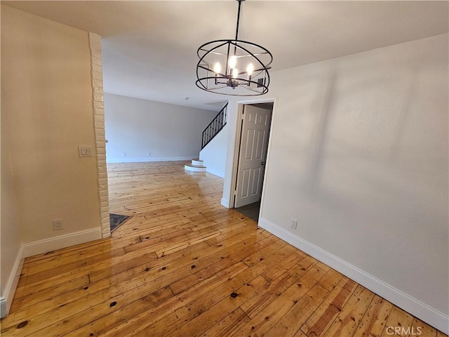 unfurnished dining area featuring a chandelier, stairway, light wood-type flooring, and baseboards