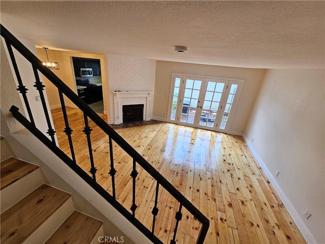 unfurnished living room featuring a brick fireplace, baseboards, hardwood / wood-style floors, french doors, and a textured ceiling