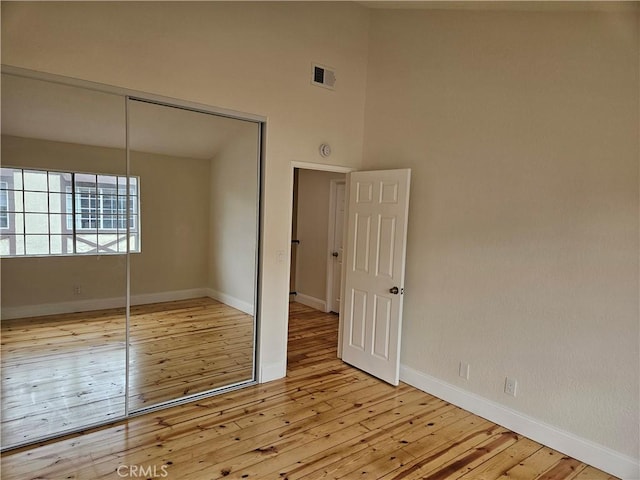 unfurnished bedroom with visible vents, light wood-style flooring, a closet, a high ceiling, and baseboards