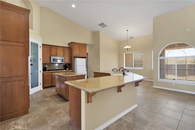 kitchen featuring pendant lighting, an island with sink, sink, white refrigerator, and an inviting chandelier