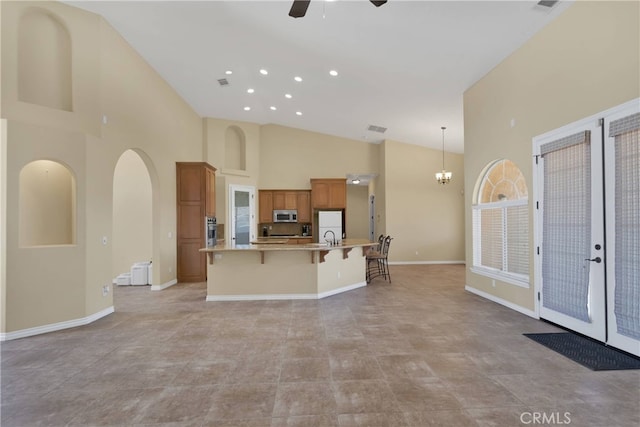 kitchen with appliances with stainless steel finishes, a towering ceiling, a breakfast bar area, a large island with sink, and hanging light fixtures