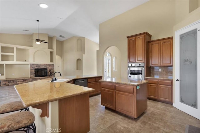 kitchen featuring a stone fireplace, black dishwasher, a kitchen island, decorative backsplash, and stainless steel oven