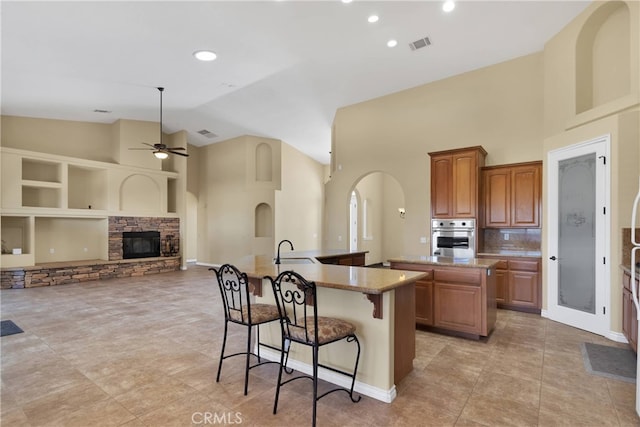 kitchen with a stone fireplace, sink, stainless steel oven, a kitchen breakfast bar, and an island with sink