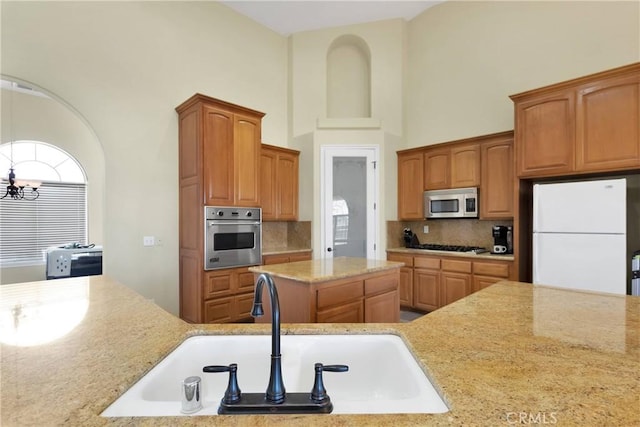 kitchen featuring sink, tasteful backsplash, light stone counters, a chandelier, and appliances with stainless steel finishes