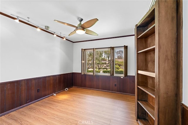 spare room featuring ornamental molding, light hardwood / wood-style floors, ceiling fan, and wooden walls