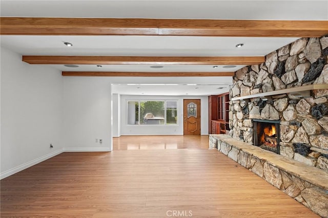 unfurnished living room with beamed ceiling, light hardwood / wood-style flooring, and a stone fireplace