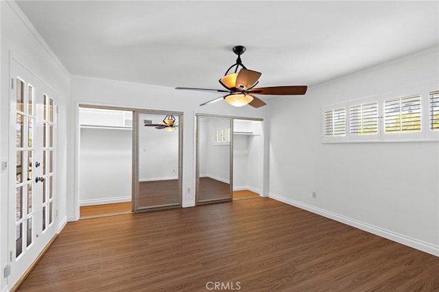 unfurnished bedroom with multiple closets, ceiling fan, dark wood-type flooring, and ornamental molding