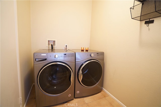 clothes washing area with laundry area, baseboards, washing machine and clothes dryer, and light tile patterned floors