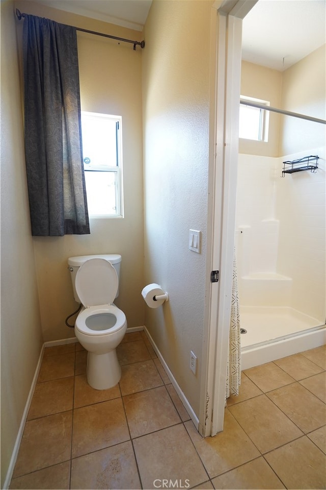 bathroom with toilet, tile patterned flooring, baseboards, and a shower stall