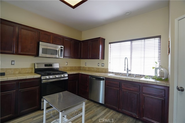 kitchen with light wood-style flooring, tile counters, appliances with stainless steel finishes, and a sink